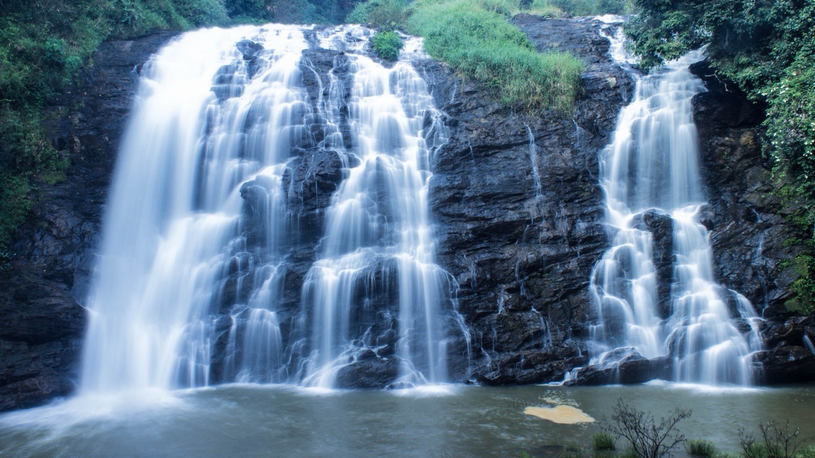 Abbey Falls spilling in several white streams over a wide, dark rock face into a pool, with green forest above