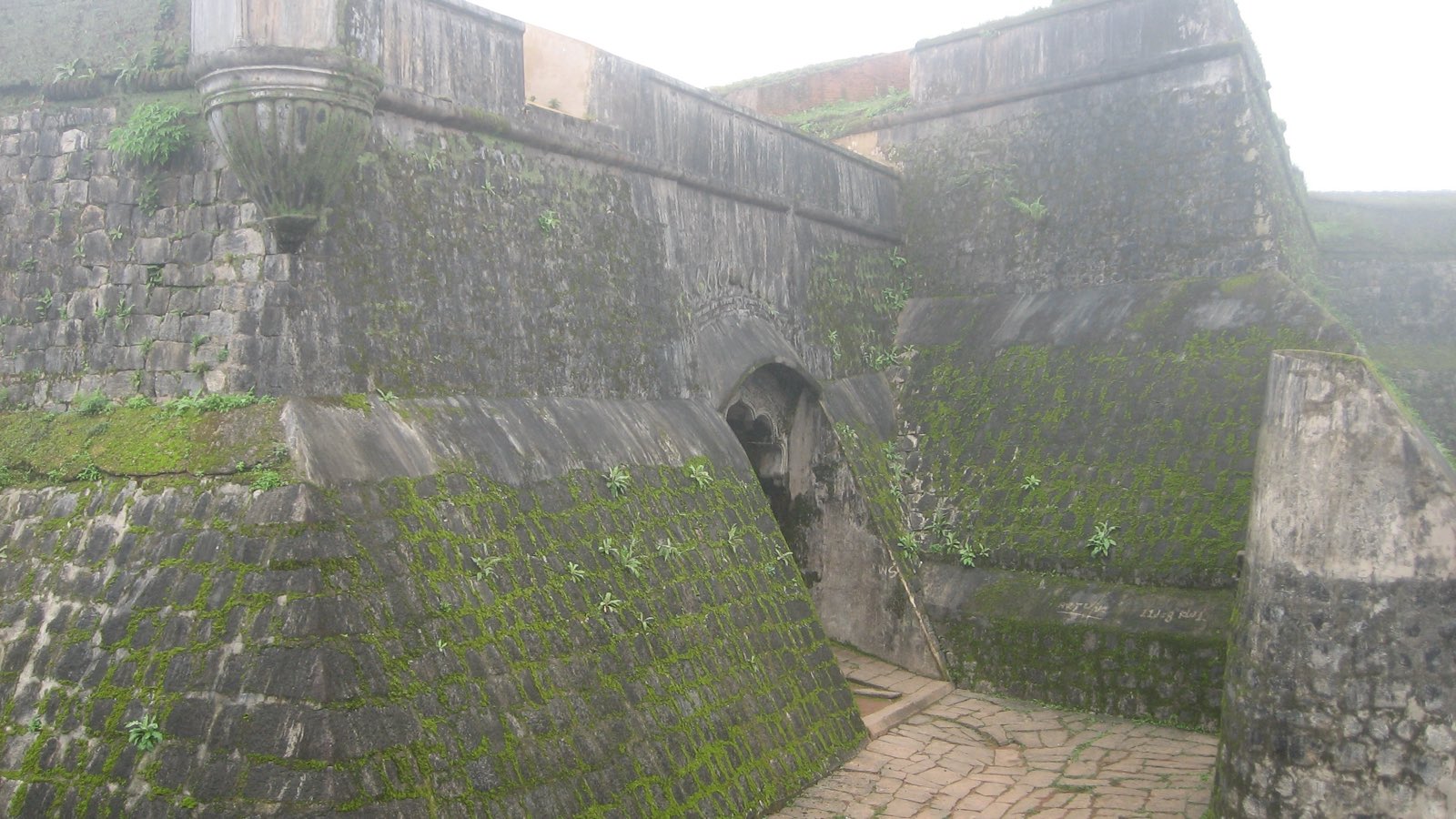Thick, moss-covered stone walls and an arched gateway at Manjarabad Fort on a misty day