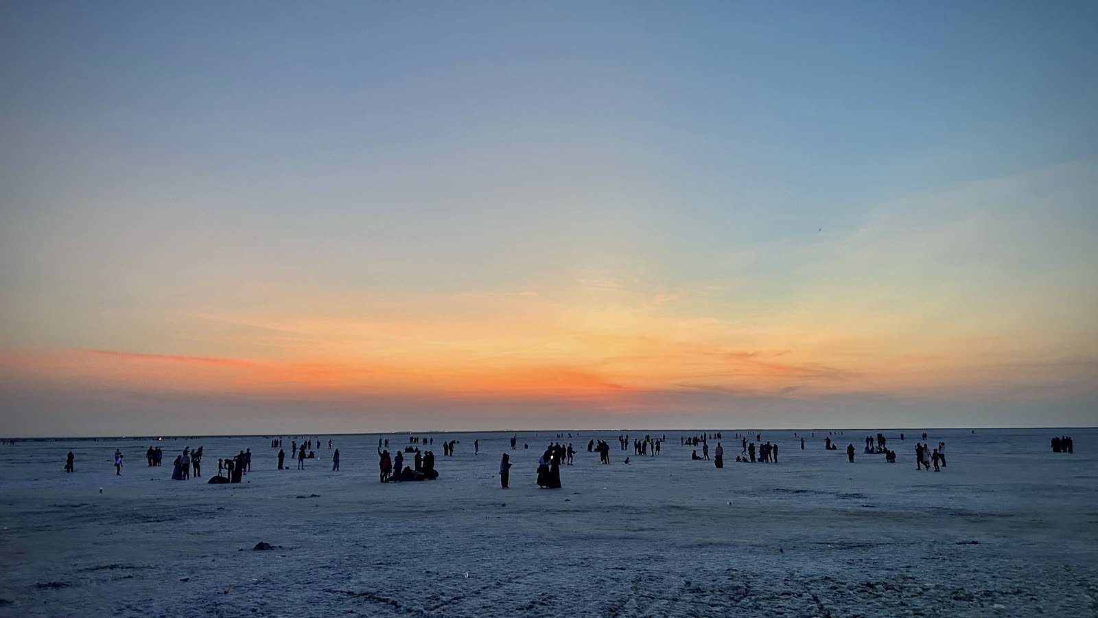 Sunset over the white salt flat of the Rann of Kutch at Dhordo, with small groups of people standing far out on the salt