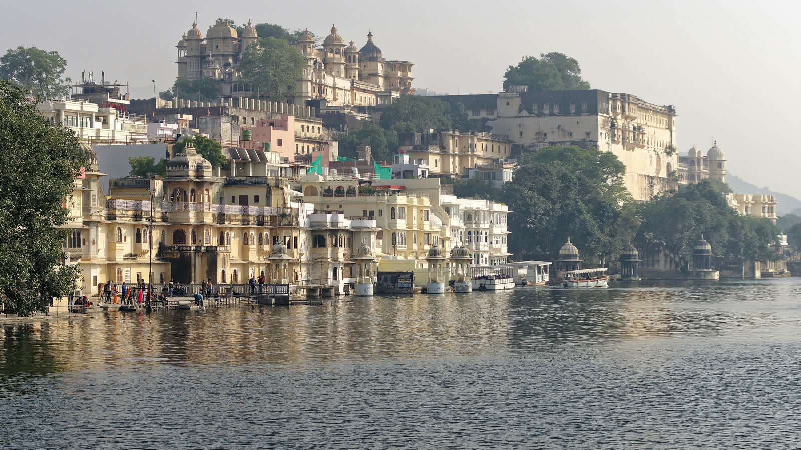 Cream-coloured palaces and old houses along the edge of Lake Pichola in Udaipur, with the domes of the City Palace on the hill above the water