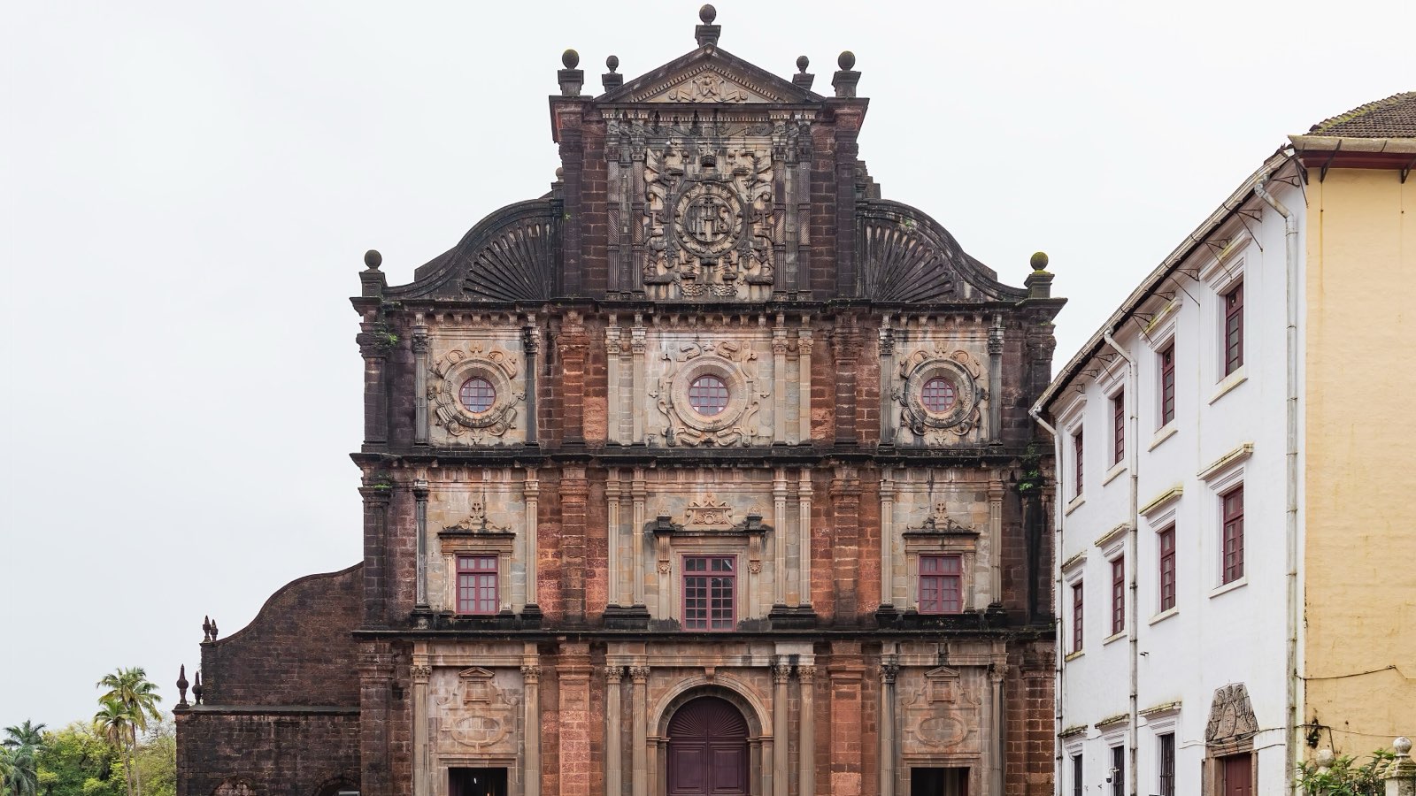The carved laterite and basalt facade of the Basilica of Bom Jesus in Old Goa under a pale sky
