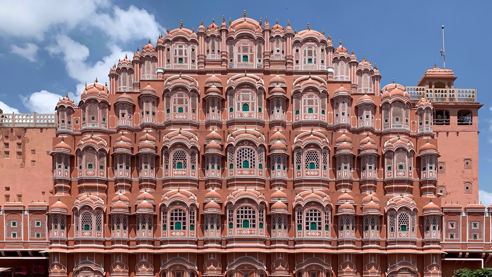 The pink sandstone facade of Hawa Mahal, rising in five storeys of small domed windows with latticed screens, against a blue sky