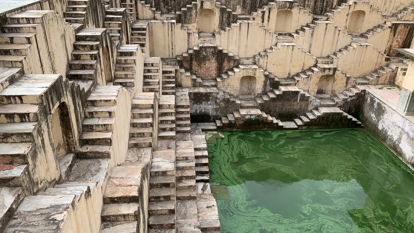 Criss-crossing flights of sandstone steps lining the sides of Panna Meena ka Kund, with green water at the bottom
