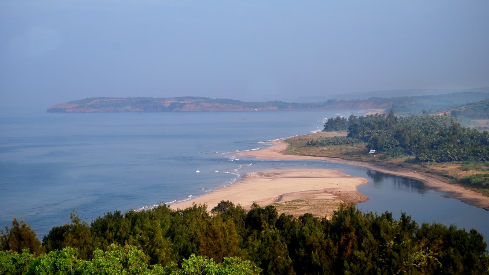 A long sandy spit, a creek and green trees on the Konkan coast at Ganpatipule, seen from above