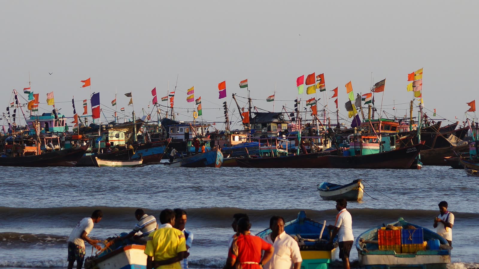 Fishing boats with colourful flags in the harbour at Harnai, with fishermen on the shore