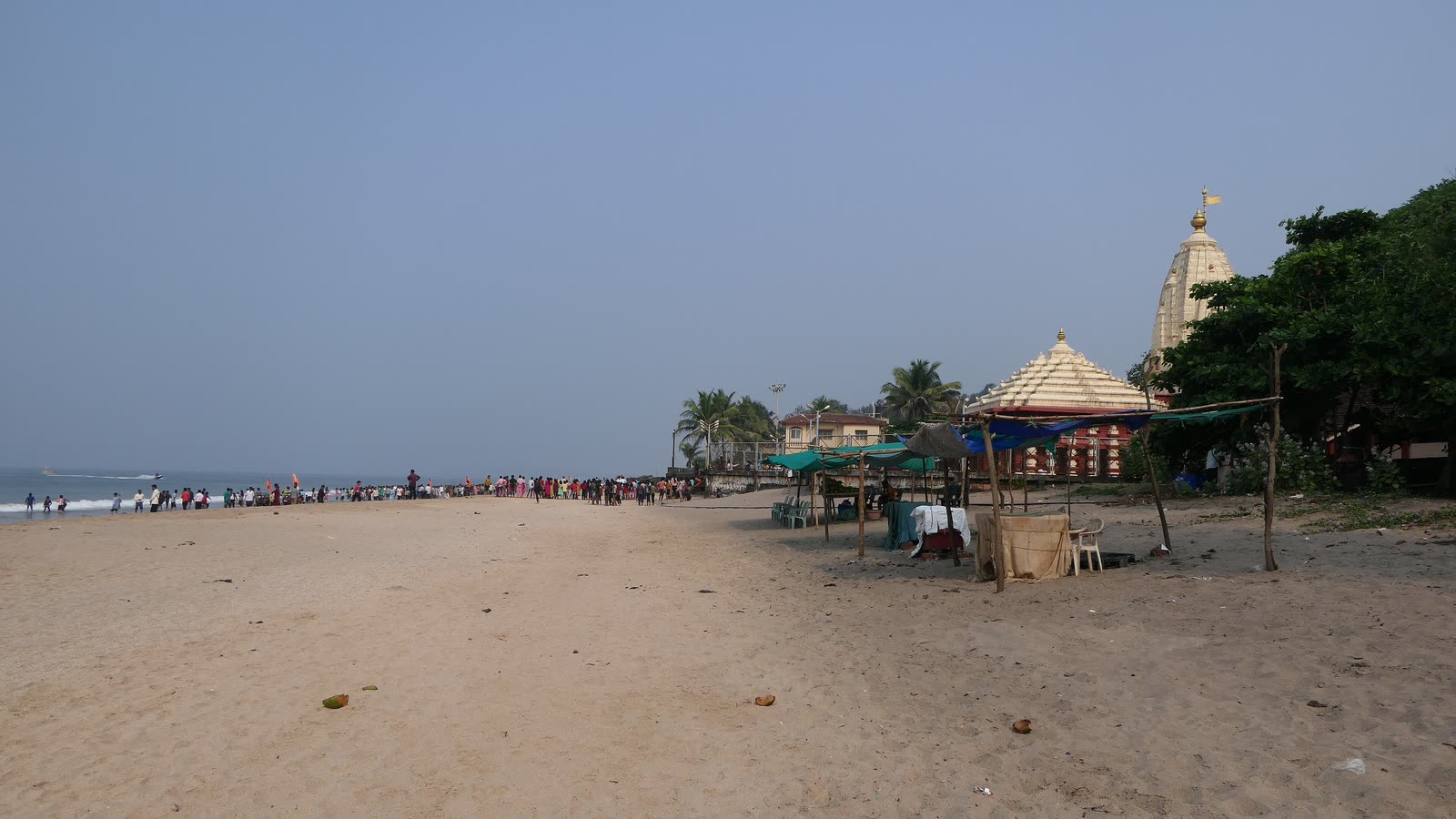 The beach at Ganpatipule, with the temple's white spire behind the stalls and trees