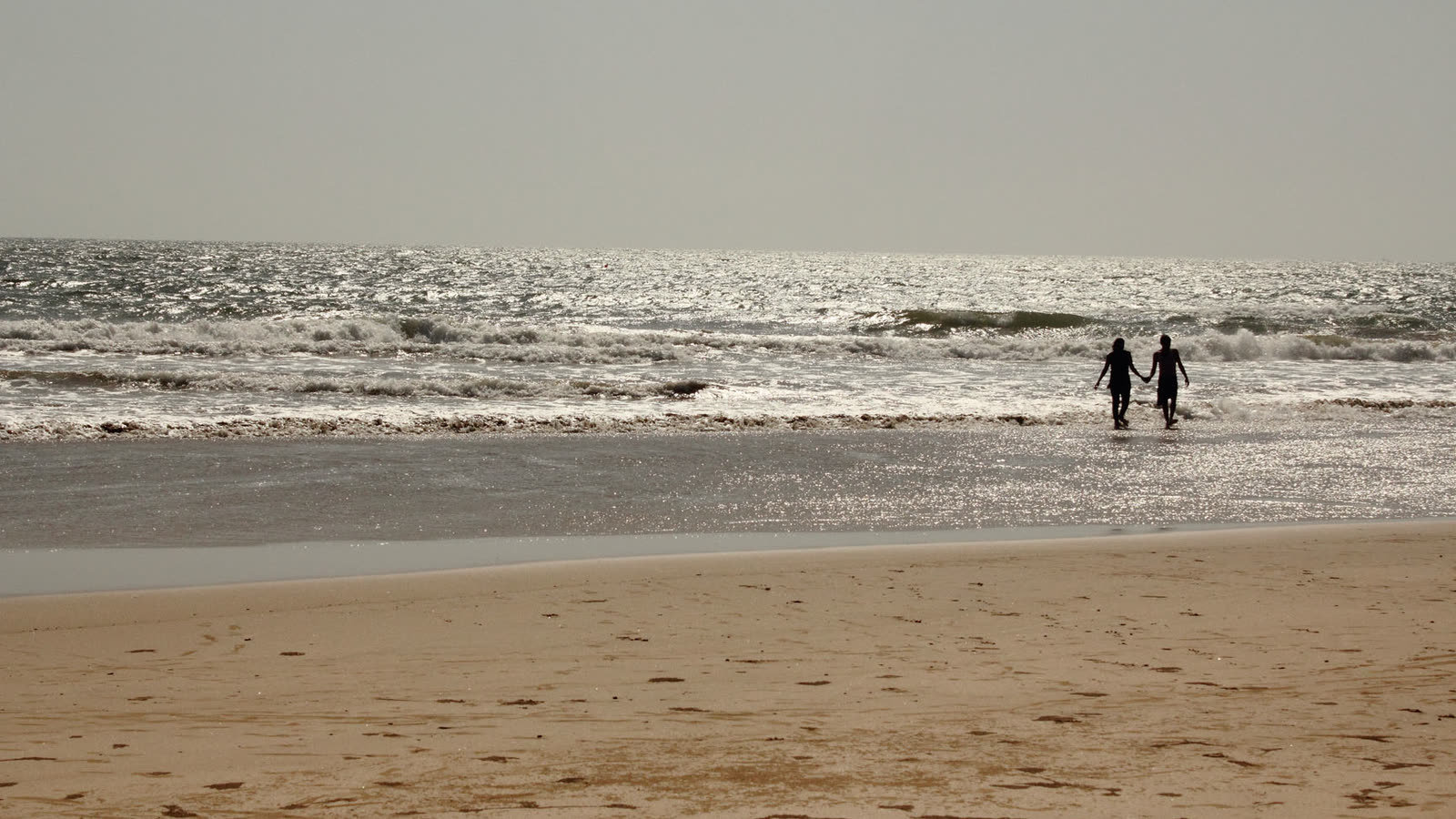Two people walking hand in hand into the waves on the long, empty beach at Guhagar