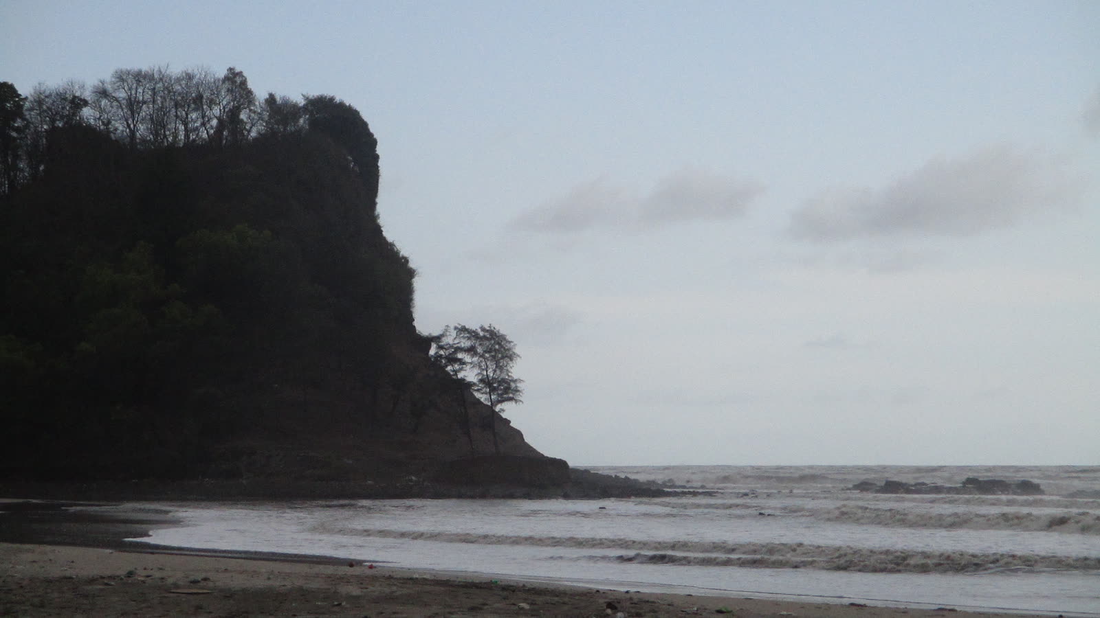 A forested headland at the end of Kashid beach, with low waves in the evening light