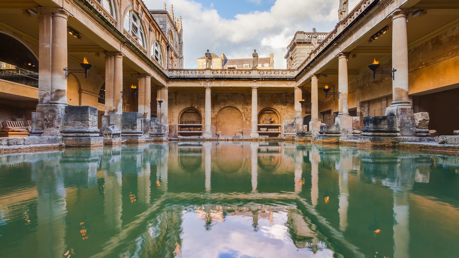 The green water of the Great Bath at the Roman Baths, surrounded by stone columns and terraces