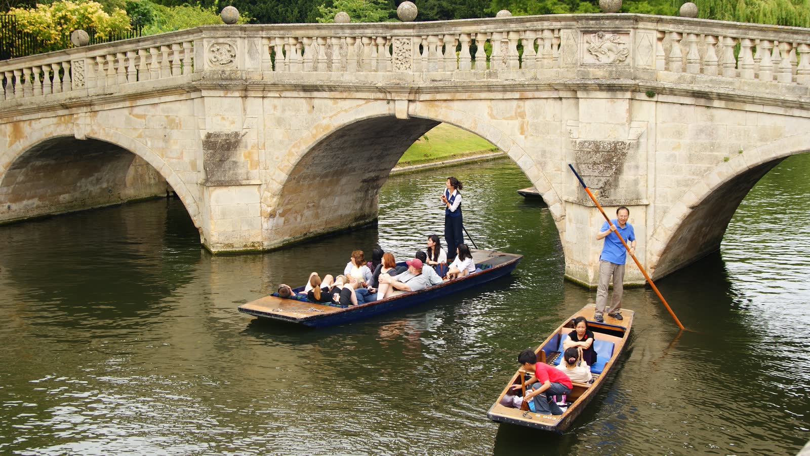 Two punts full of people on the River Cam passing under an old stone bridge
