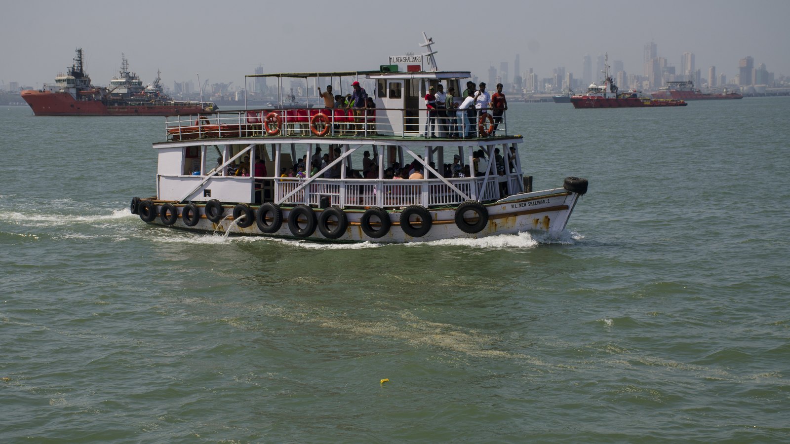 A double-decker ferry crossing Mumbai harbour towards Elephanta, with the city skyline behind