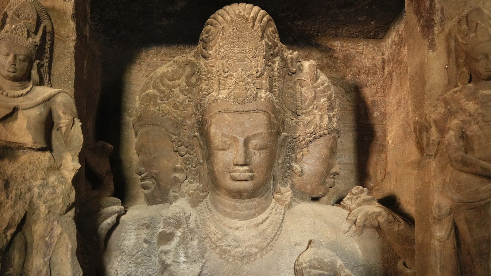 The huge three-headed Shiva carved into the rock of the main cave at Elephanta, lit from the side