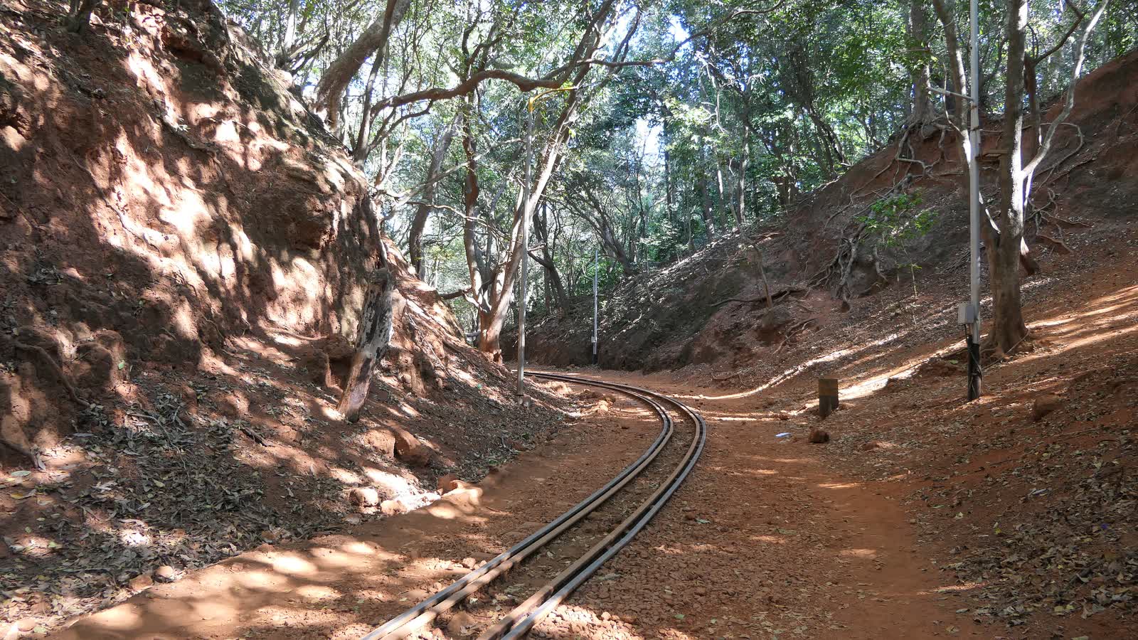 The narrow-gauge toy train track curving through a red earth cutting in the forest at Matheran
