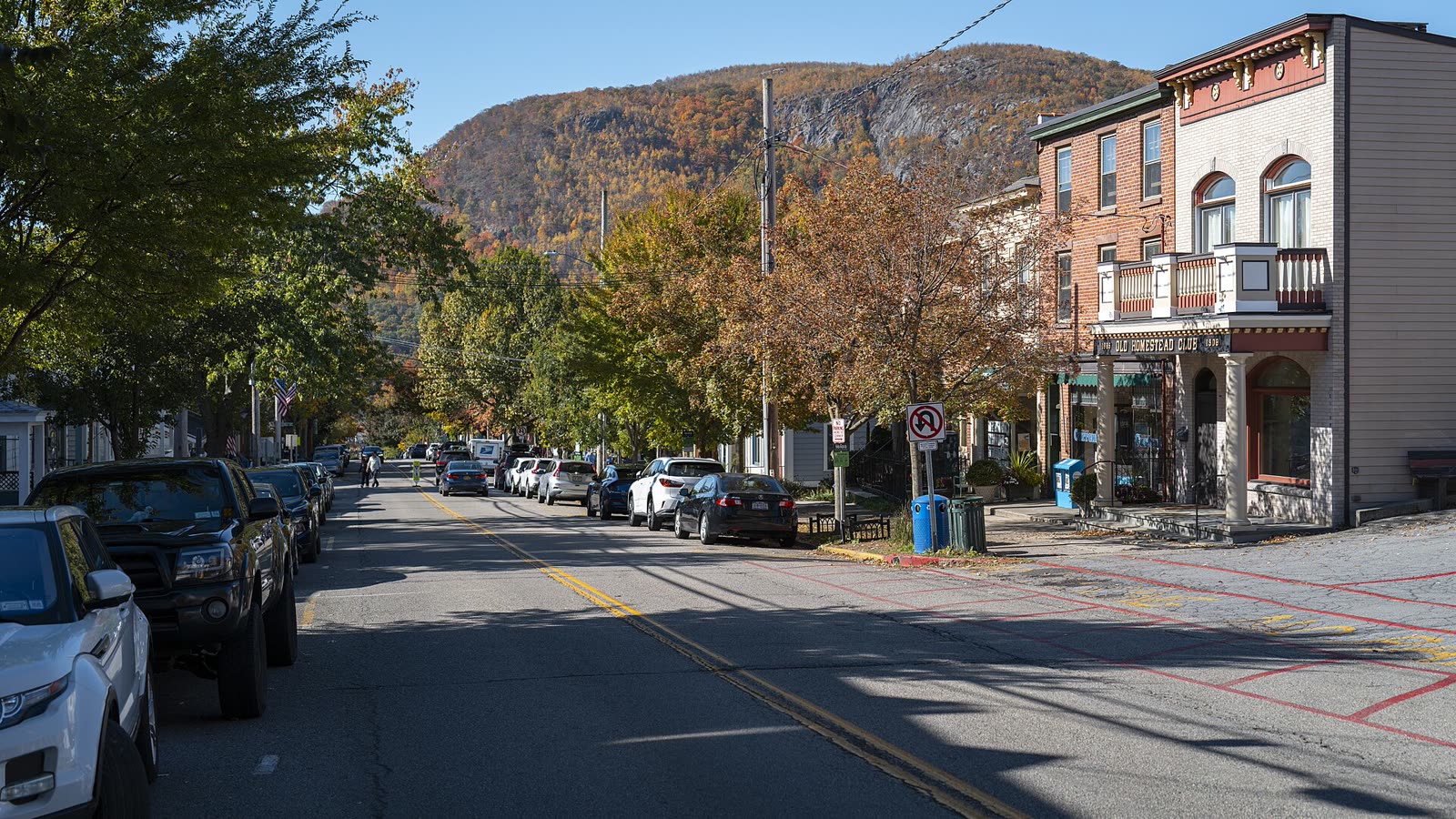 Cold Spring's Main Street with brick buildings, autumn trees and a wooded mountain behind