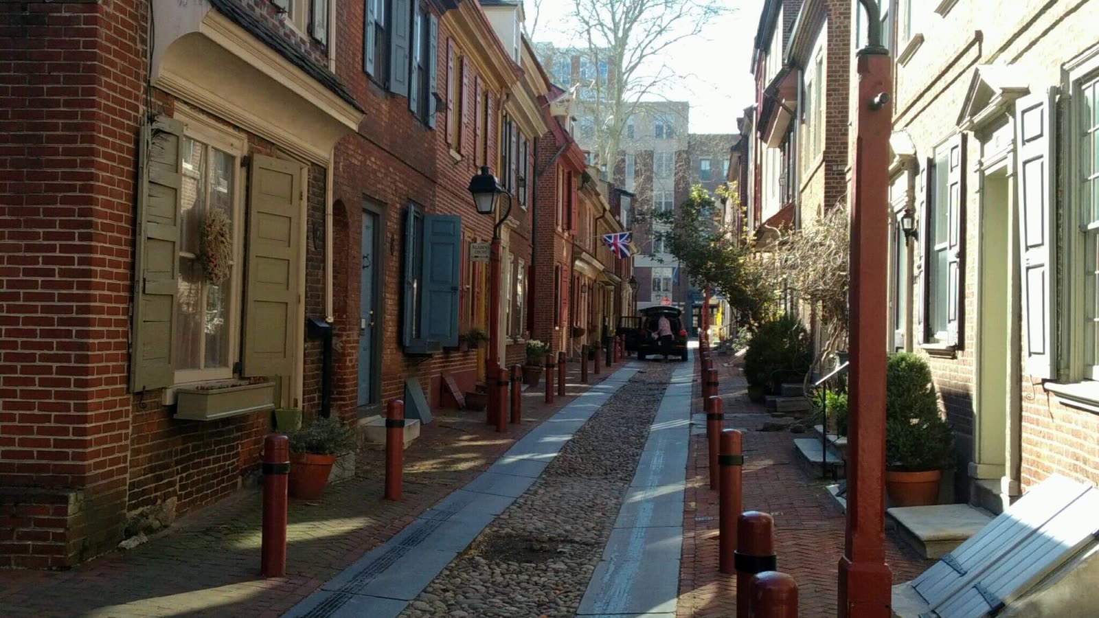 A narrow cobbled street lined with old brick row houses and flower pots