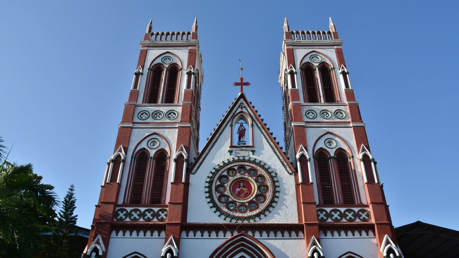 The twin towers of the Basilica of the Sacred Heart of Jesus, red and white Gothic-style stonework around a round rose window, against a blue sky