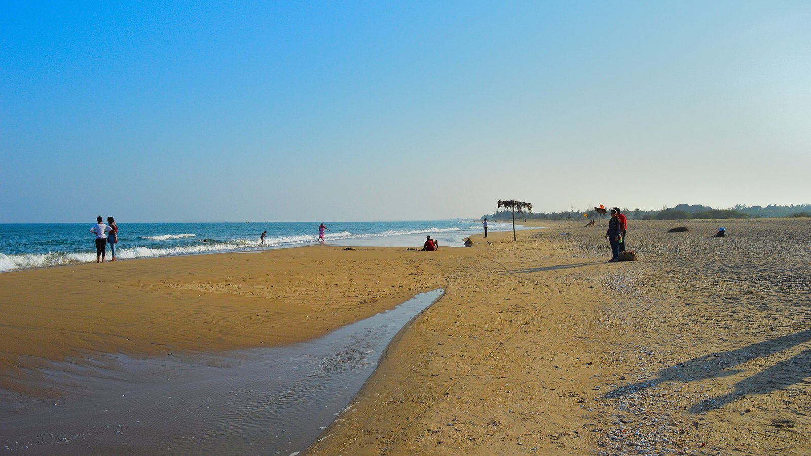 A long golden sandbar at Paradise Beach with a shallow channel of water in the foreground and the sea on the left under a clear blue sky
