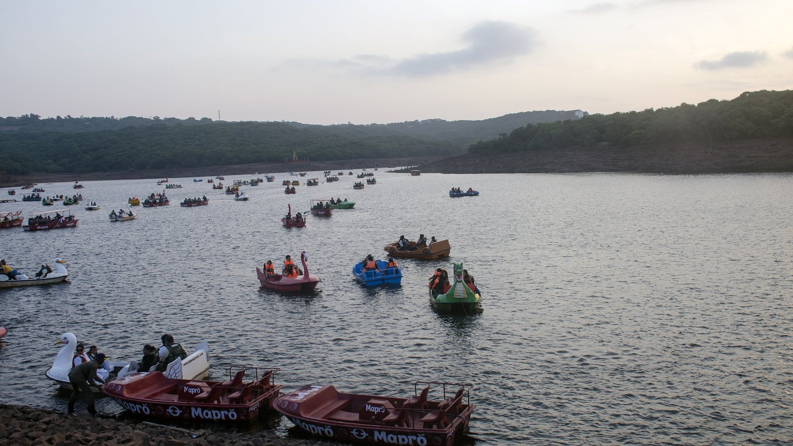 Colourful pedal boats on Venna Lake in the evening, with wooded hills around the water