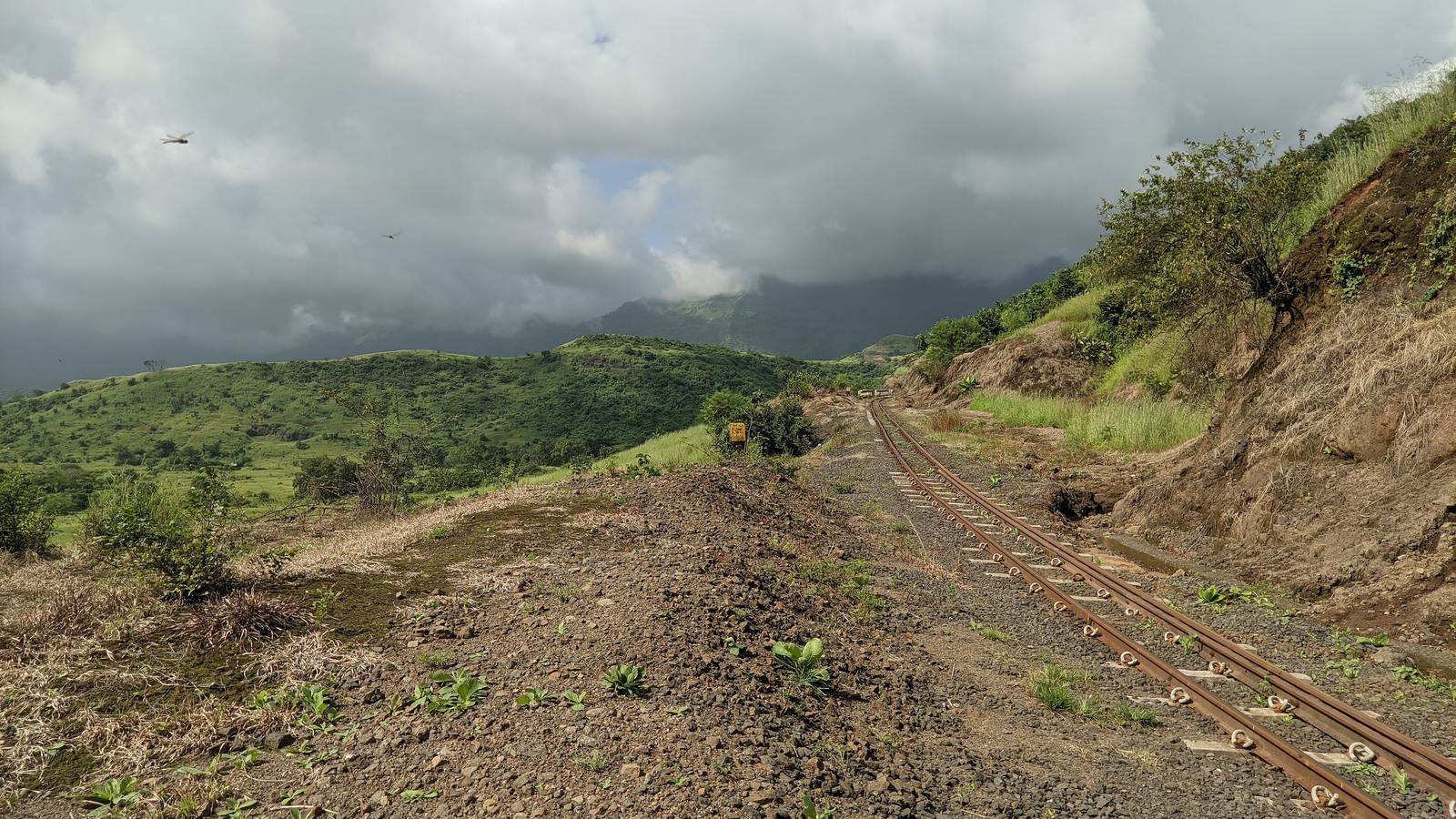 The narrow-gauge toy train line running along a red earth hillside, with clouds over the green hills of Matheran