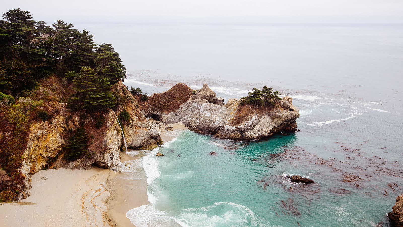 McWay Falls dropping onto a small sandy cove of turquoise water below forested cliffs