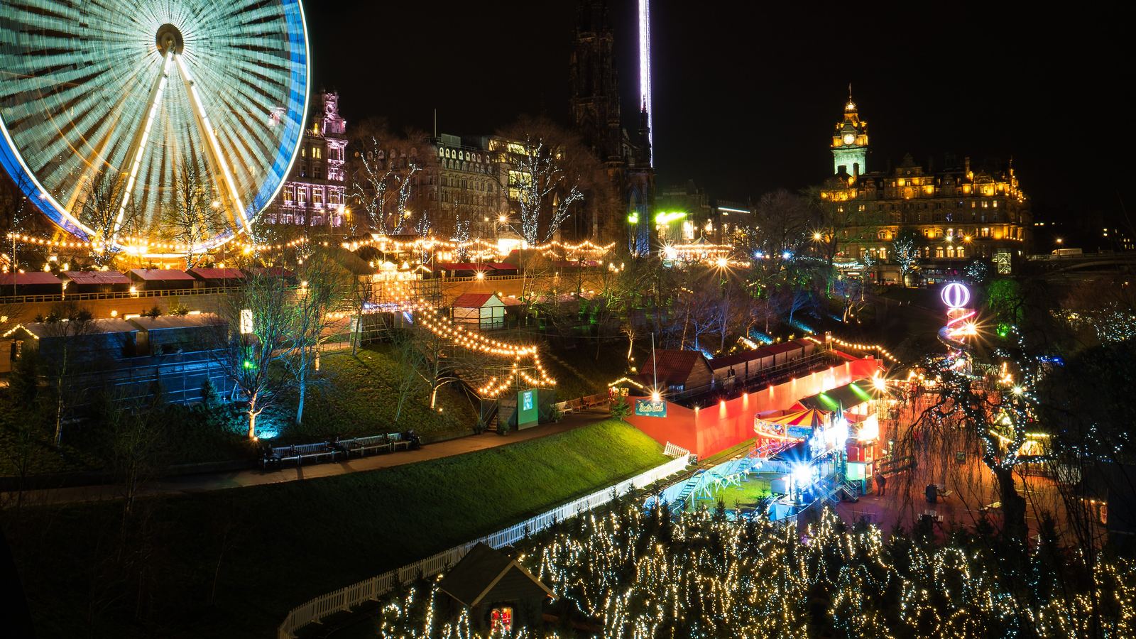 The Big Wheel lit up at night above the Christmas market and fairground rides in Princes Street Gardens, Edinburgh, with the Balmoral clock tower behind