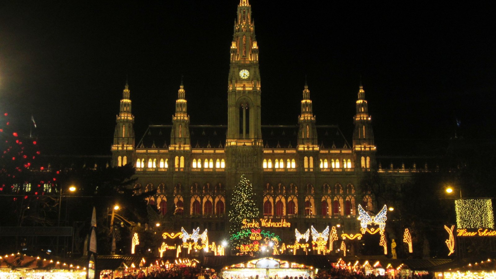 Vienna City Hall lit up at night, with a Christmas tree and the lights of the market stalls on Rathausplatz in front